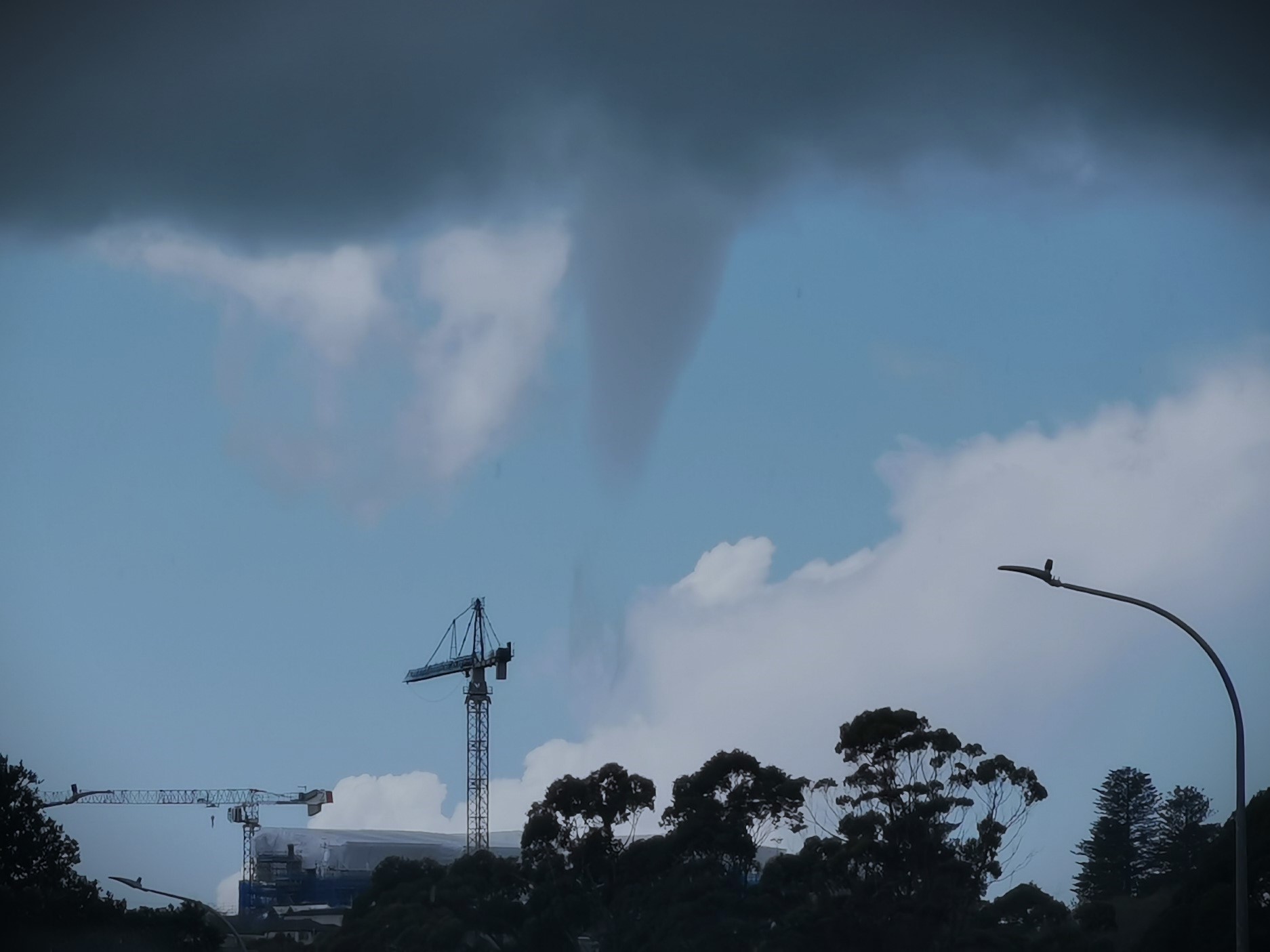 Funnel cloud formation coming out from dark clouds against the blue sky behind